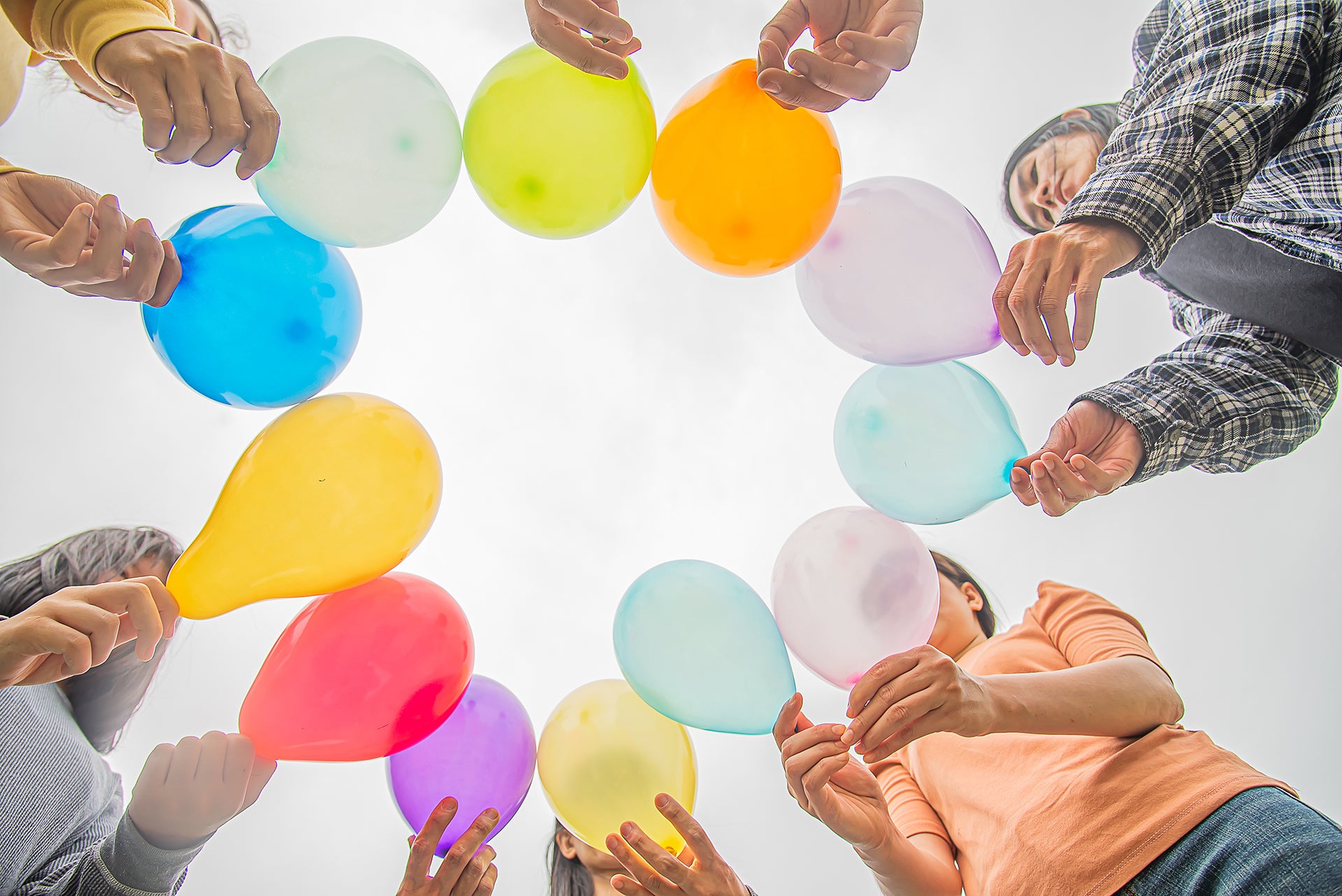 Diverse Gruppe hält bunte Luftballons kreisförmig nach oben, Blick von unten